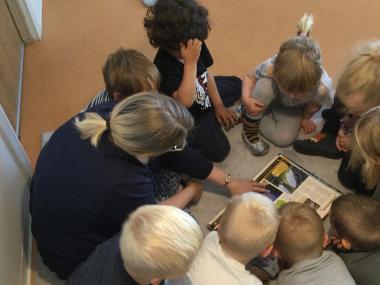 Voksen læser og snakker med en gruppe børn på gulvet.